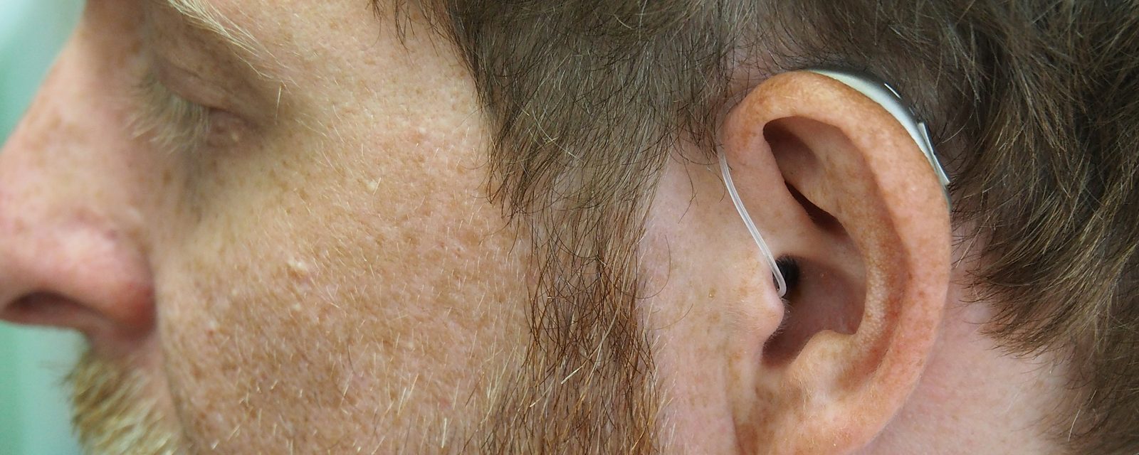 A close-up of a man wearing a receiver-in-canal hearing aid, the thin wire running over his ear and into the canal